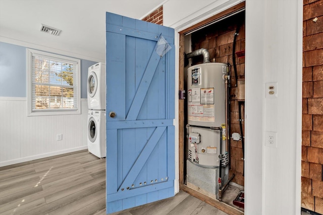 washroom with stacked washing maching and dryer, hardwood / wood-style floors, and gas water heater