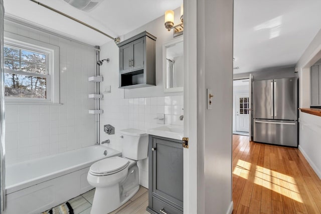 full bathroom with toilet, tile walls, vanity, tiled shower / bath combo, and hardwood / wood-style flooring