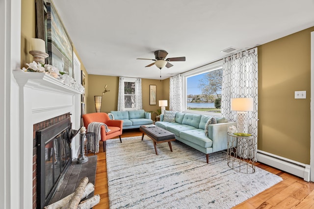 living area featuring a baseboard heating unit, wood finished floors, a brick fireplace, a ceiling fan, and baseboards