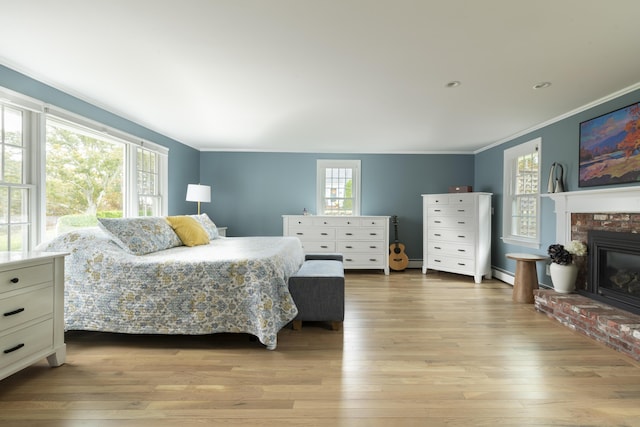 bedroom with a brick fireplace, baseboard heating, multiple windows, and light wood-type flooring