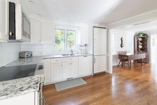 kitchen featuring light stone countertops, white cabinetry, sink, backsplash, and light hardwood / wood-style flooring