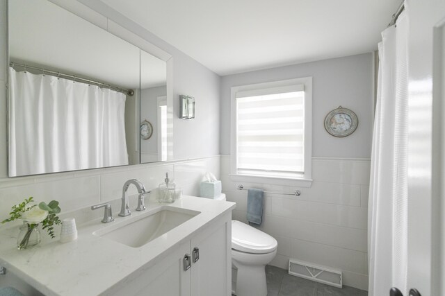 bathroom featuring toilet, vanity, tile patterned floors, and tile walls