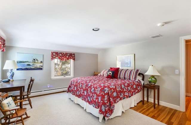 bedroom with a baseboard radiator, visible vents, baseboards, and wood finished floors