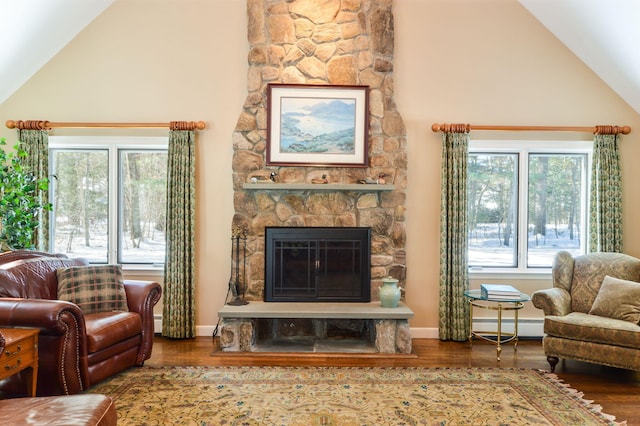 living area with a wealth of natural light, a baseboard heating unit, wood finished floors, and a stone fireplace