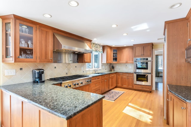 kitchen with stainless steel appliances, glass insert cabinets, a peninsula, and exhaust hood