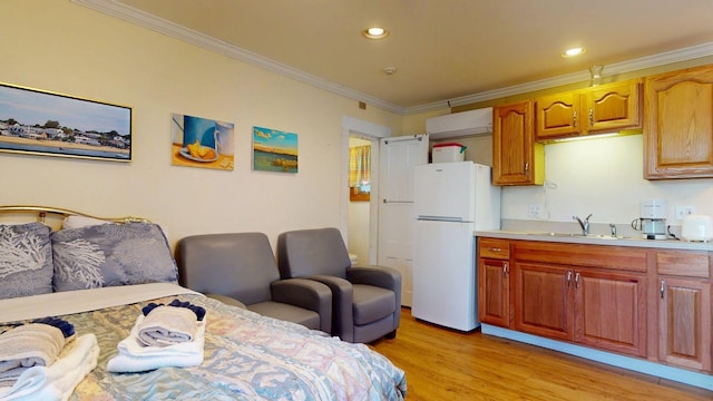 interior space with a sink, light wood-type flooring, freestanding refrigerator, crown molding, and light countertops