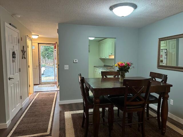 dining area featuring a textured ceiling, dark wood-style flooring, and baseboards