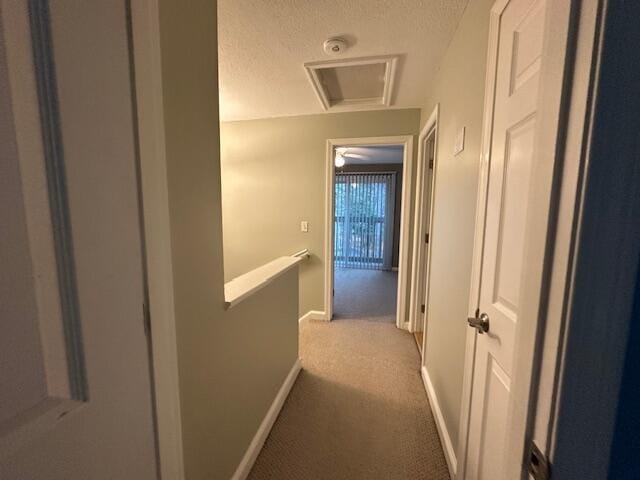 hallway featuring carpet floors, attic access, an upstairs landing, baseboards, and a textured ceiling