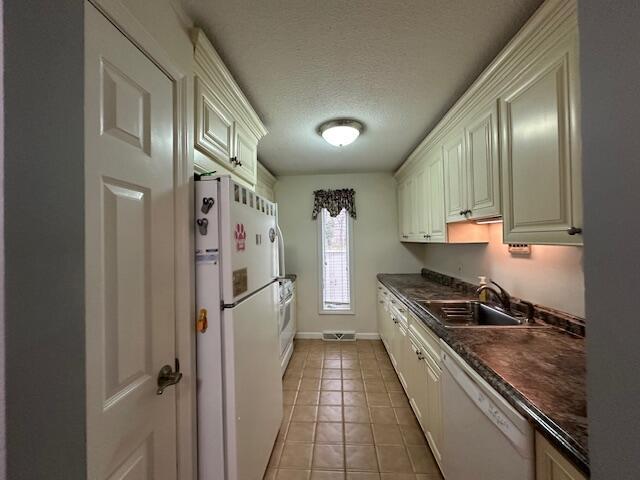 kitchen featuring white appliances, dark countertops, a sink, a textured ceiling, and light tile patterned flooring