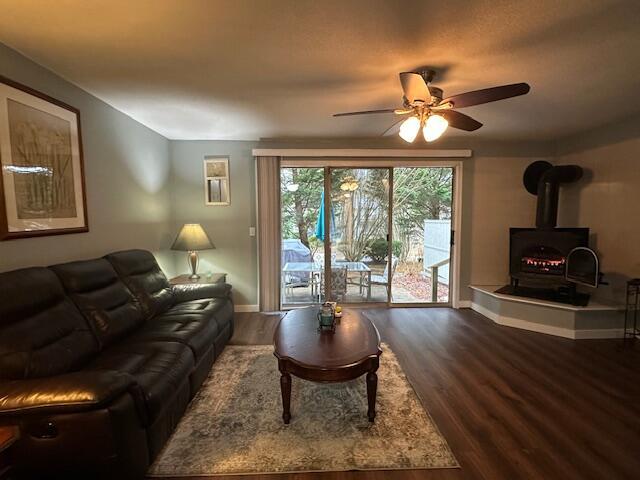 living room featuring baseboards, a wood stove, wood finished floors, and ceiling fan