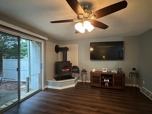 living area featuring a wood stove, a ceiling fan, visible vents, baseboards, and wood finished floors
