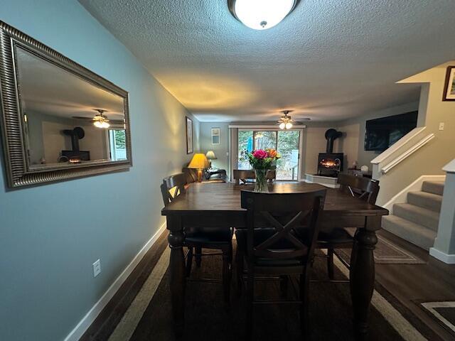 dining room featuring baseboards, a wood stove, a ceiling fan, and a textured ceiling