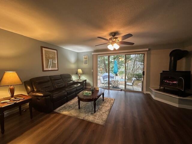 living room with a wood stove, a ceiling fan, wood finished floors, and baseboards