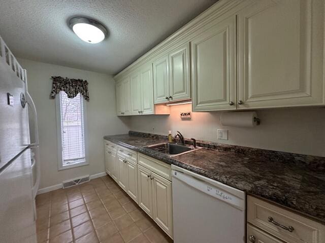 kitchen with a sink, visible vents, freestanding refrigerator, baseboards, and white dishwasher