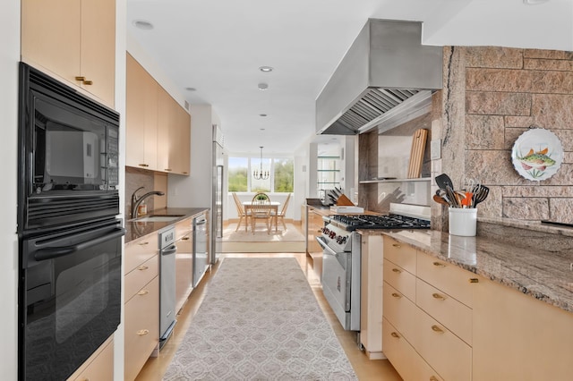 kitchen featuring appliances with stainless steel finishes, wall chimney range hood, sink, hanging light fixtures, and light stone counters