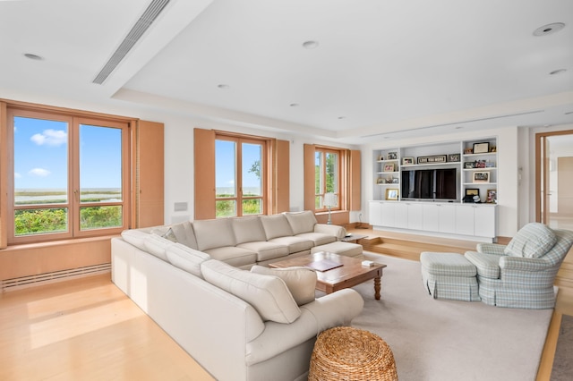 living room with built in features, a raised ceiling, light hardwood / wood-style flooring, and a baseboard radiator