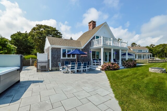 back of property featuring a balcony, a yard, a patio area, and a hot tub