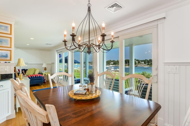 dining room with light hardwood / wood-style floors, crown molding, a water view, and an inviting chandelier