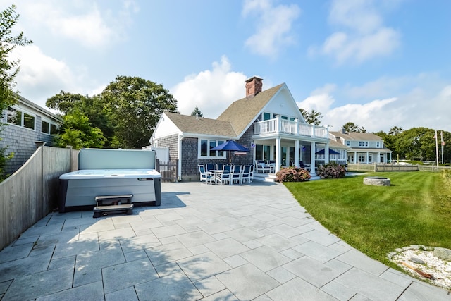 rear view of property with a balcony, a patio area, a hot tub, and a yard