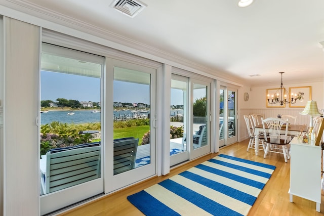 doorway to outside featuring crown molding, an inviting chandelier, a water view, and light hardwood / wood-style flooring