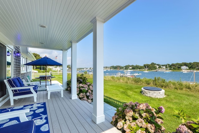 deck with a water view, a lawn, and a fire pit