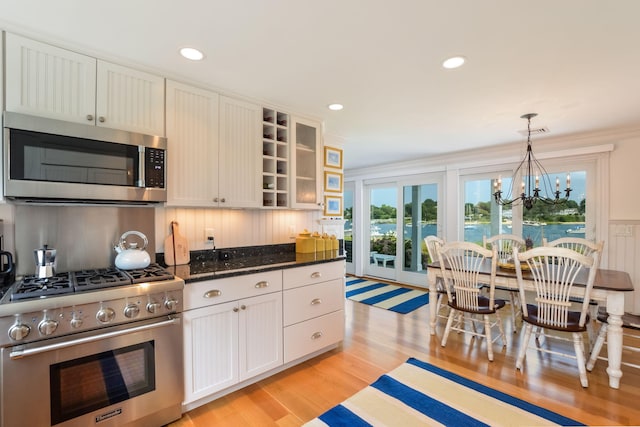 kitchen featuring pendant lighting, white cabinetry, stainless steel appliances, dark stone counters, and ornamental molding