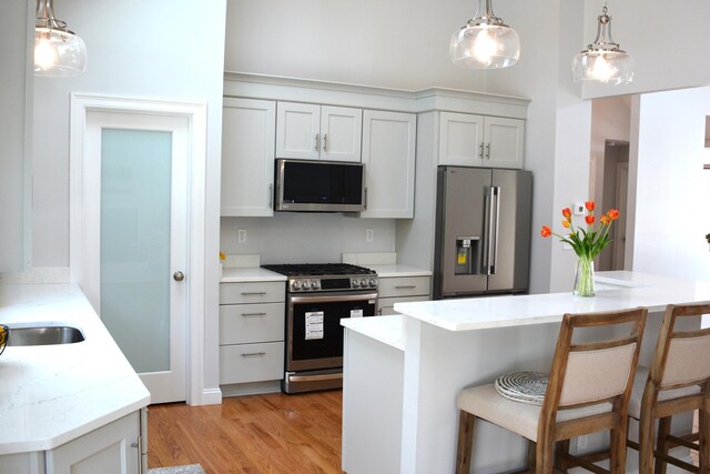 55 Blue Castle Dr, Mashpee, MA 02649 - kitchen with appliances with stainless steel finishes, light wood-type flooring, a kitchen breakfast bar, hanging light fixtures, and light stone countertops