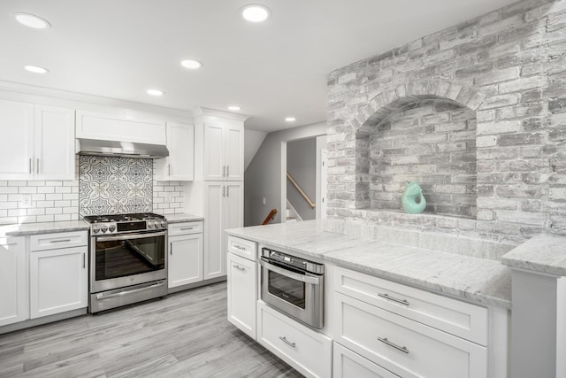 46 Juniper Ln W, South Chatham, MA 02659 - kitchen featuring light stone countertops, white cabinetry, under cabinet range hood, appliances with stainless steel finishes, and backsplash