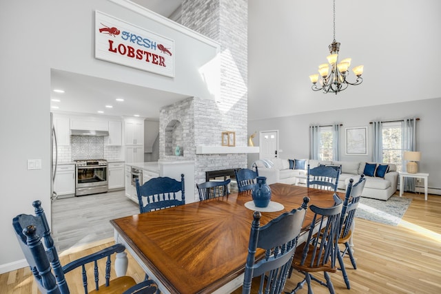 46 Juniper Ln W, South Chatham, MA 02659 - dining room featuring a brick fireplace, a towering ceiling, baseboards, light wood finished floors, and a notable chandelier