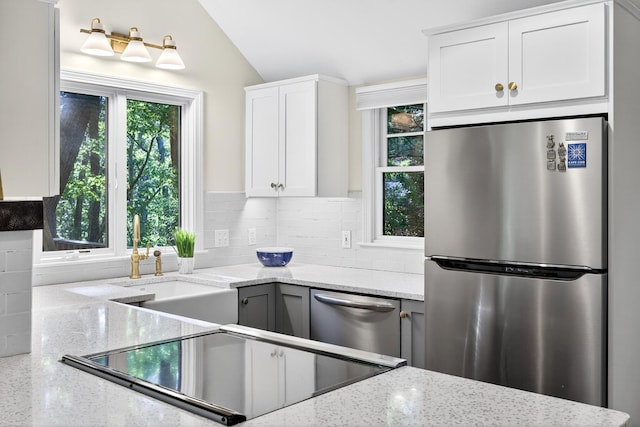 50 Piper Ln, Eastham, MA 02642 - kitchen featuring stainless steel appliances, light stone countertops, backsplash, vaulted ceiling, and white cabinetry