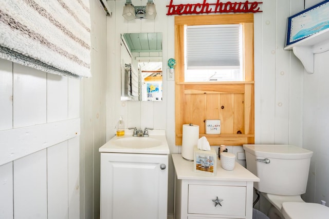 bathroom featuring wood walls, a healthy amount of sunlight, toilet, and vanity