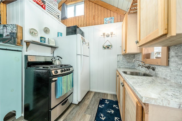 kitchen with stainless steel range with gas stovetop, vaulted ceiling, sink, light wood-type flooring, and wooden walls