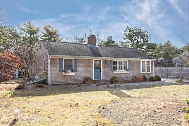 ranch-style house featuring a front lawn, a shingled roof, a chimney, and fence