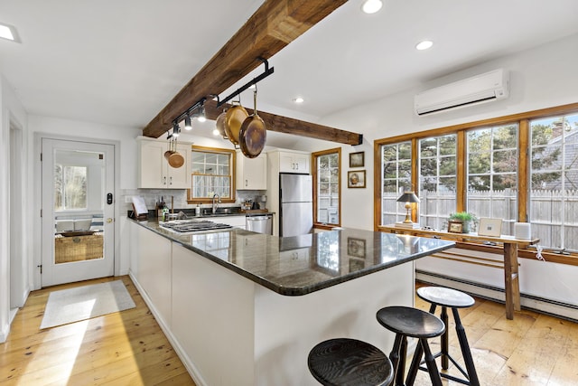 kitchen with an AC wall unit, a healthy amount of sunlight, tasteful backsplash, and stainless steel appliances