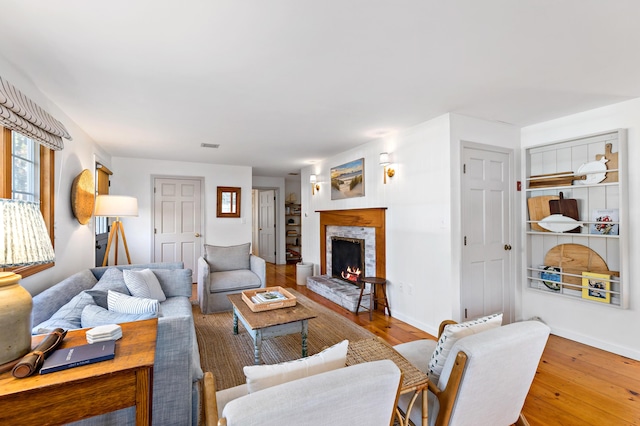 living room with baseboards, wood-type flooring, a stone fireplace, and visible vents