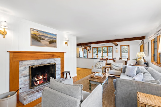 living area featuring beamed ceiling, a warm lit fireplace, and wood finished floors