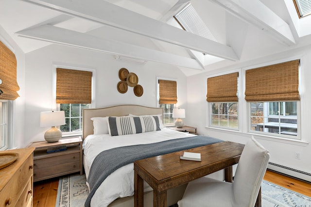 bedroom with lofted ceiling with skylight, a baseboard heating unit, and wood finished floors