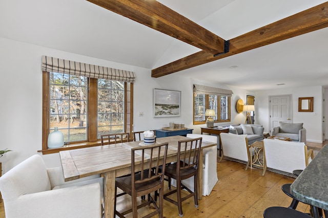 dining room featuring light wood-type flooring and vaulted ceiling with beams