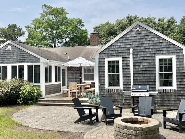 rear view of property featuring a fire pit, a shingled roof, a chimney, and a patio area