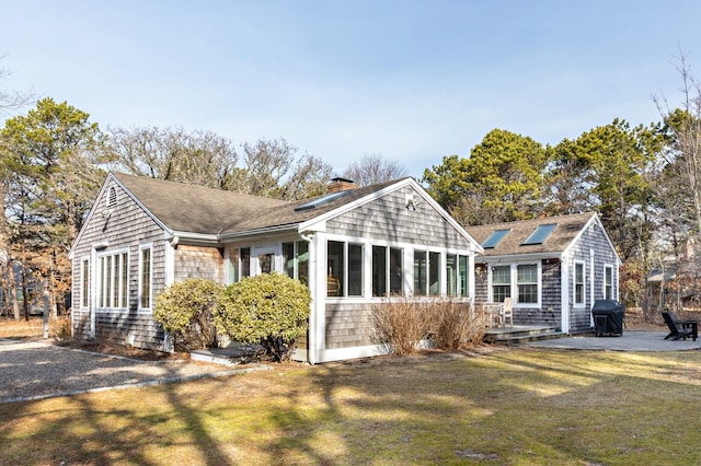 rear view of house with a lawn, a patio, roof with shingles, a sunroom, and a chimney