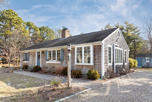 ranch-style house with a storage shed, an outdoor structure, roof with shingles, and a chimney