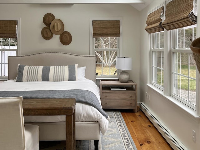 bedroom with vaulted ceiling, baseboards, wood-type flooring, and a baseboard radiator