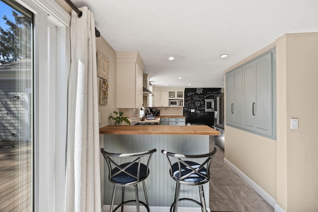 kitchen featuring butcher block countertops, a sink, stainless steel appliances, wall chimney range hood, and baseboards