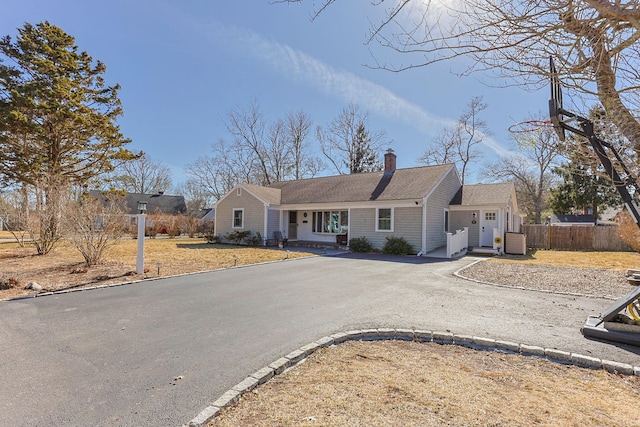 ranch-style home featuring a shingled roof, driveway, a chimney, and fence