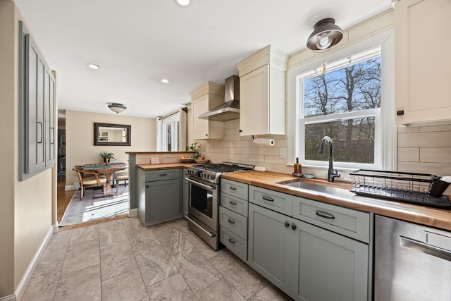 kitchen featuring appliances with stainless steel finishes, wood counters, wall chimney range hood, and a sink