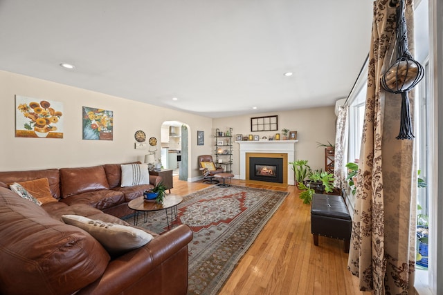 living room with recessed lighting, arched walkways, a fireplace with flush hearth, and light wood finished floors