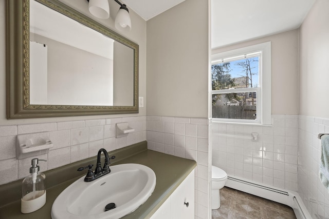 bathroom with a wainscoted wall, toilet, vanity, baseboard heating, and tile walls