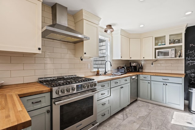 kitchen with appliances with stainless steel finishes, wooden counters, wall chimney range hood, and a sink