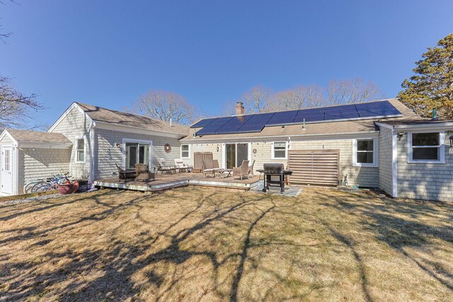 back of house featuring a deck, an outbuilding, a lawn, and roof mounted solar panels