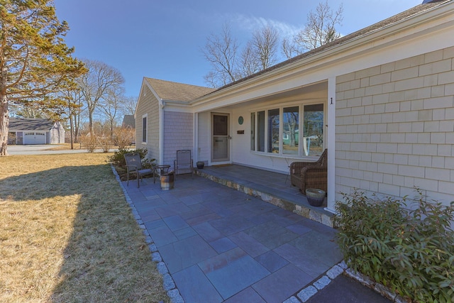 view of exterior entry featuring a patio, a yard, and a shingled roof